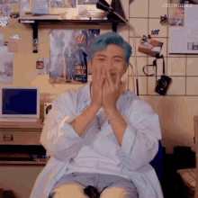 a man with blue hair is sitting in front of a wall that has a poster that says angels like you