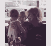 a woman is holding a baby while sitting at a table in front of a window .