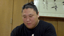 a man with a bun on his head is sitting in front of a wall with a picture on it .
