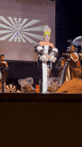a drag queen stands on a stage in front of a screen that says ' a ' on it