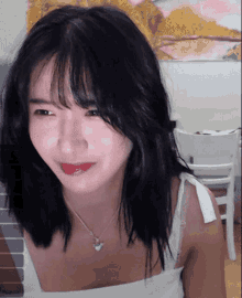 a woman wearing a white tank top and a heart shaped necklace