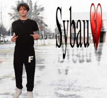 a young man in a black shirt and black sweatpants stands in front of a sybau logo