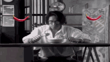 a man is sitting at a table with a bowl of food and two red peppers are behind him