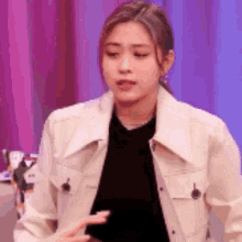 a woman in a white jacket is standing in front of a pink curtain .