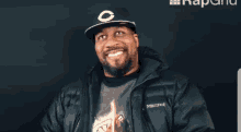 a man wearing a black jacket and a black hat is laughing .