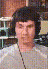 a man wearing headphones is looking at the camera with a cat in the background