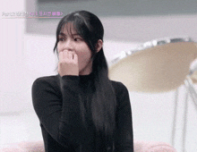 a woman with long black hair is covering her mouth with her hand .