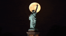 the statue of liberty is lit up at night with a full moon behind her .