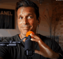 a man holds an orange microphone in front of a sign that says channel