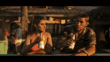 a man and a woman sitting at a table drinking corona