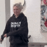 a woman wearing a donut shop hoodie is standing in front of a painting .