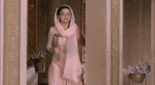 a woman in a pink dress and scarf is standing in a room holding a hammer .