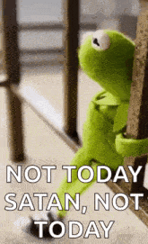 kermit the frog is sitting on a railing with the words `` not today satan , not today '' written on it .