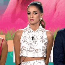 a woman in a white crop top stands in front of a pink backdrop
