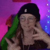 a woman wearing a black beanie and glasses is giving a thumbs up sign .