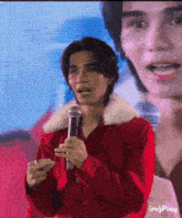 a man in a red jacket is holding a microphone and talking into it .