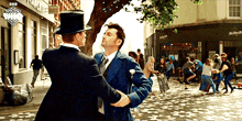 a man in a top hat talks to another man in a blue suit