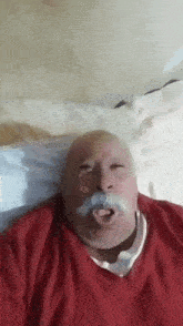 a man with a mustache and a red sweater is laying on a bed