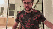 a man wearing glasses and a floral shirt is standing in front of a mirror in a room .