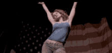 a woman in a blue tank top is dancing in front of a large american flag
