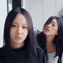 a woman with long black hair is standing next to another woman with shorter hair