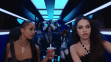 a woman holding a cup with a straw in it stands next to another woman