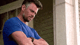a man with a beard is standing on a porch with his arms crossed and looking down .