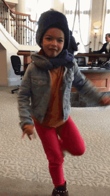 a little girl wearing a denim jacket and red pants is standing on one leg