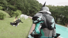 a man in a batman costume is standing in the grass near a swimming pool
