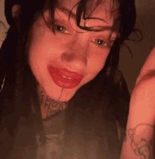 a close up of a woman with red lipstick and a tattoo on her neck .