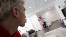 a man in a red shirt is sitting in a living room looking out the window