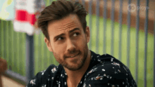a man with a beard wearing a floral shirt is sitting on a bench looking at the camera .