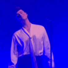 a man in a white shirt is standing on a stage in front of a microphone with his hands on his hips .