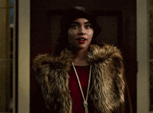a woman wearing a fur coat and a red dress is standing in front of a door .