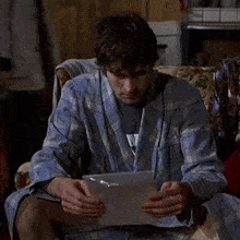 a man in a plaid robe is sitting on a couch reading a magazine