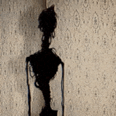 a statue of a skeleton is standing in front of a wall with a pattern