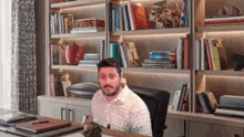 a man is sitting at a desk in front of a bookshelf with books on it .