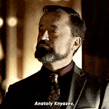 a man with a beard wearing a suit and tie says " anatolay knyazev "