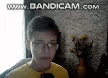 a boy wearing glasses and a yellow shirt is sitting in front of a window .