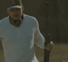 a man wearing a white shirt and a camo hat holds a gun in his right hand