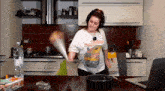 a woman wearing headphones is standing in a kitchen next to a laptop and a bottle of water .