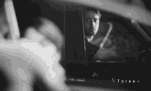 a black and white photo of a man in a car with toree written on the bottom right