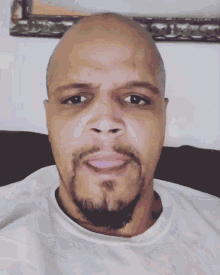 a bald man with a beard wearing a white shirt looks at the camera
