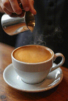 a person is pouring milk into a cup of cappuccino
