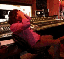 a woman in a pink shirt sits in a recording studio with her hands on her head