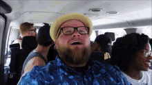 a man with a beard wearing glasses and a hat is sitting in a car