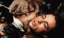 a man is kissing another man on the cheek while they are laying down .