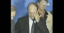 a man in a suit and tie is covering his face with his hands while standing next to another man .