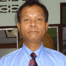 a man wearing a blue shirt and a red and black tie is looking at the camera .