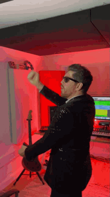 a man in a suit and sunglasses is playing a guitar in a studio